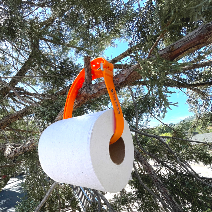 White camping toilet with orange handle hanging from a tree