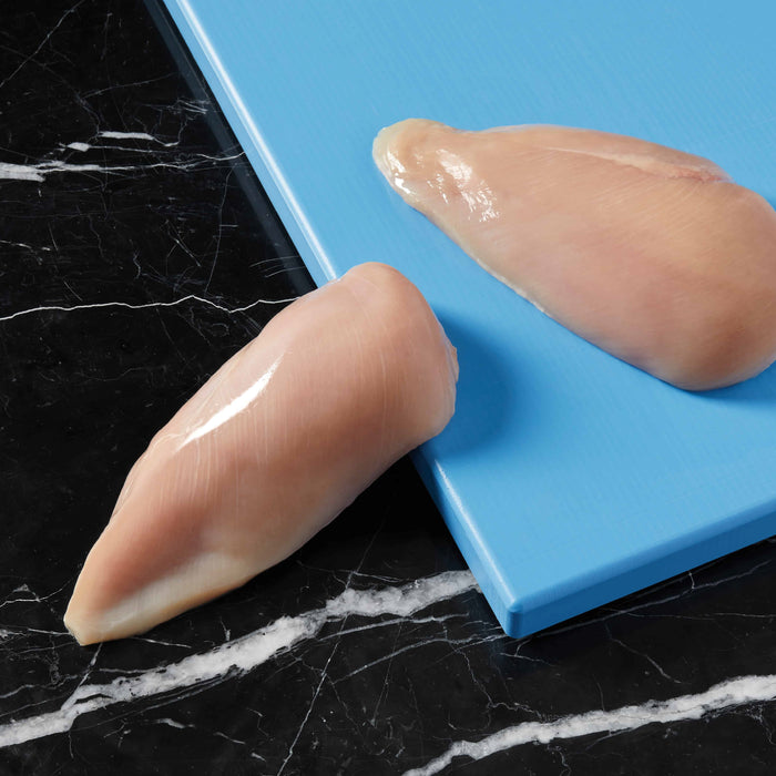 Two high-quality chicken breasts—one on a blue cutting board, the other on black marble—perfect for preparing Cat Person Chicken Paté, a protein-rich cat food.