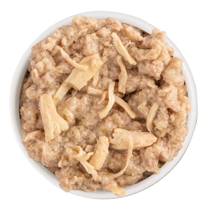 A white bowl filled with Dogs in the Kitchen Fowl Ball, featuring shredded cage-free chicken in a creamy sauce, is shown from above on a white background.