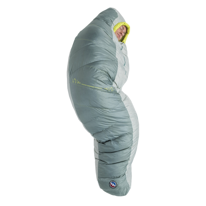 A person stands upright, fully zipped inside the Big Agnes Returns Sidewinder 0˚ sleeping bag in gray and light green, featuring body-mapped insulation with only their face visible.
