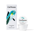 A box and cup of Cat Person Tuna Paté cat food are pictured, with a blue and green fish illustration on the packaging. The box showcases balanced nutrition along with product details and nutritional info in black text.